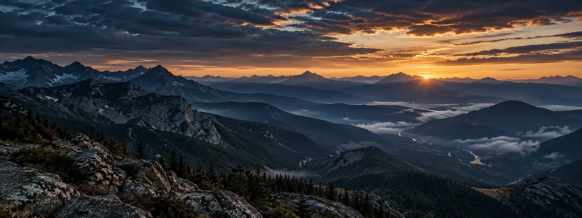 Layered mountain range at blue hour with warm light breaking across the horizon.